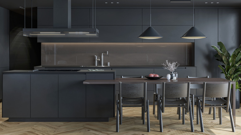 Sleek kitchen with dark cabinets, countertops, and fixtures with an island connected to a dark wood dining table