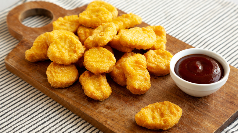 Chicken nuggets on wood board with sauce in a small white bowl