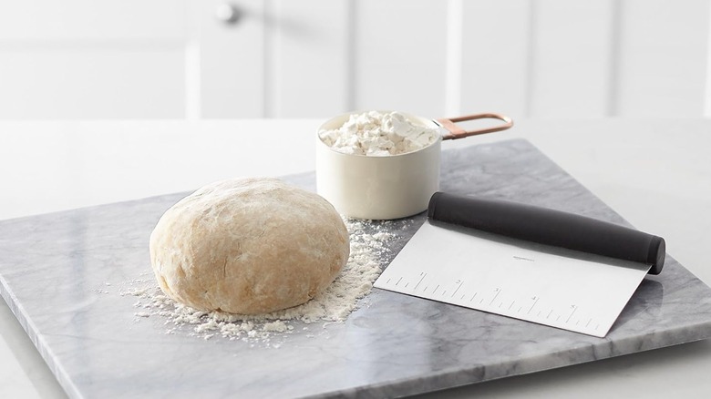 dough, scraper, cup of flour on marble board