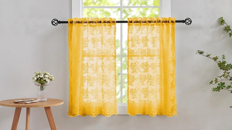 Yellow lace curtains hanging on window with table in foreground