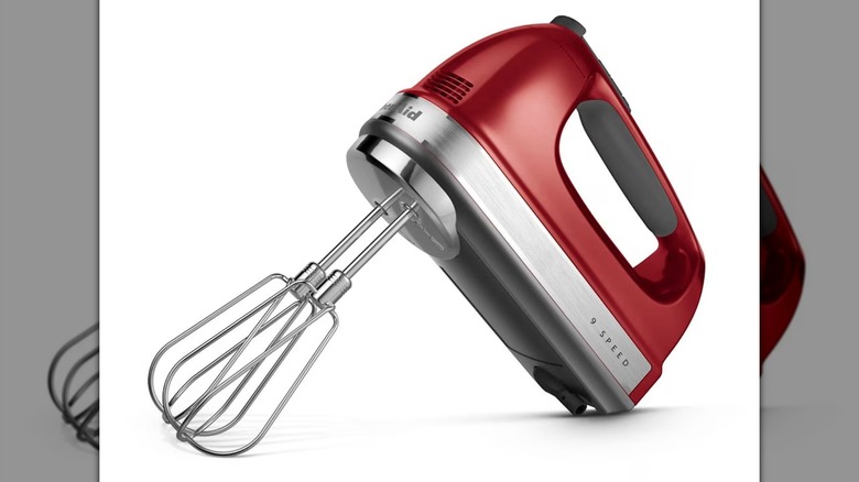 A red KitchenAid 9-Speed Hand Mixer with whisk attachments on a white background