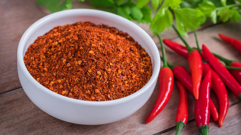 Ground cayenne pepper in a white bowl next to red chile peppers