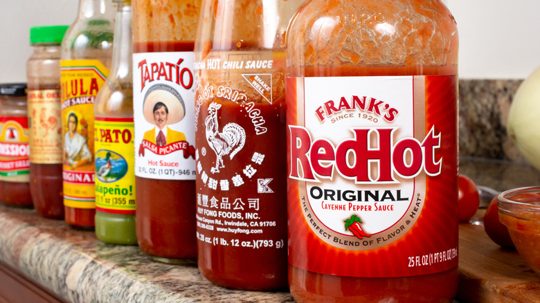 A shelf of assorted hot sauces including sriracha, Cholula, and Frank's Red Hot