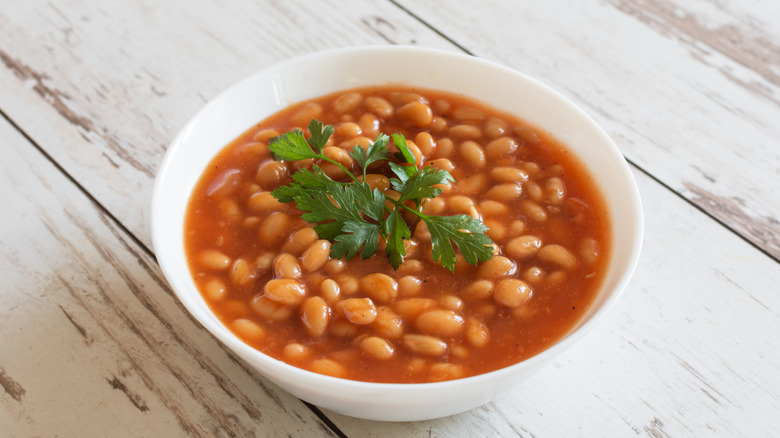 A white bowl of canned baked beans garnished with cilantro
