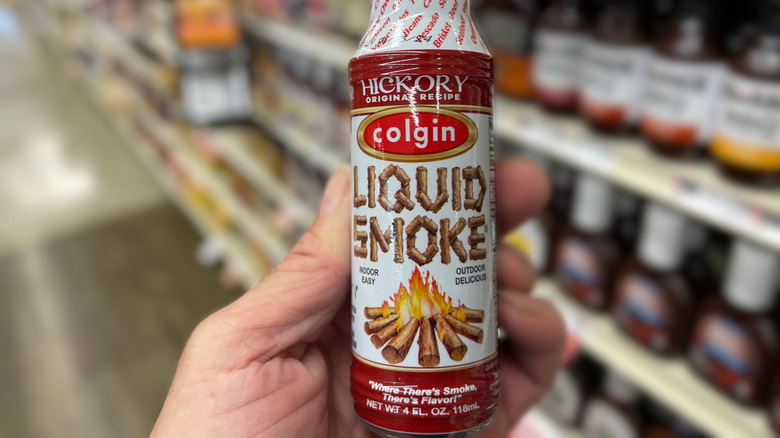 A hand holding a bottle of Colgin Hickory Liquid Smoke