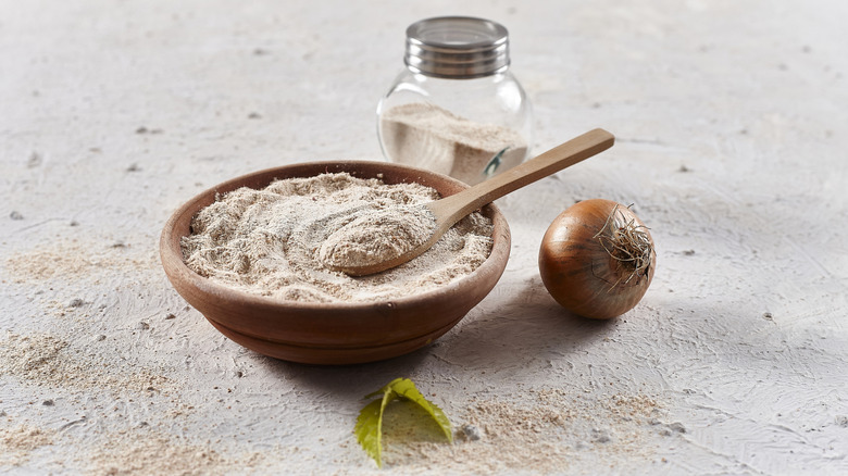 A wooden bowl of onion powder with a white onion nearby