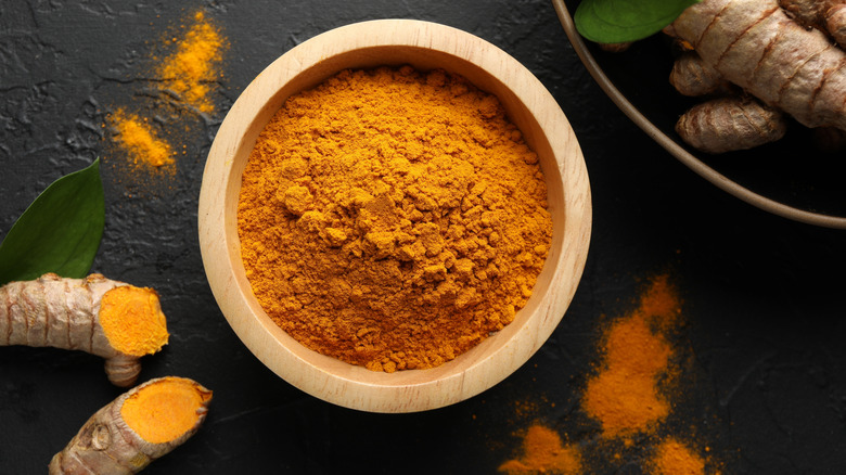 Turmeric powder in a small bowl, with sliced turmeric root and leaves to the side