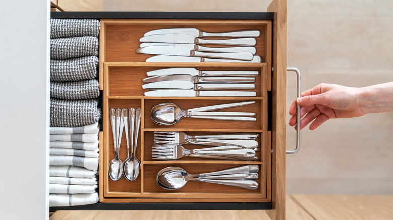 Hand pulling out organized kitchen cutlery drawer