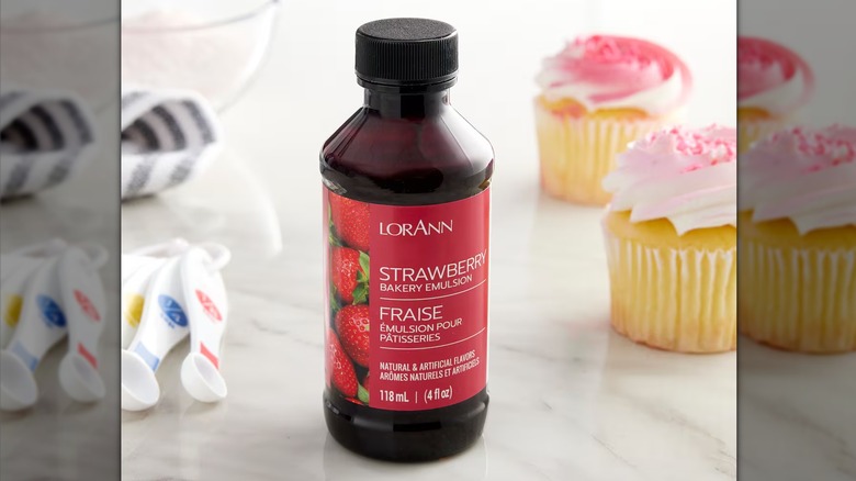Bottle of lorann strawberry emulsion next to measuring spoons and cupcakes