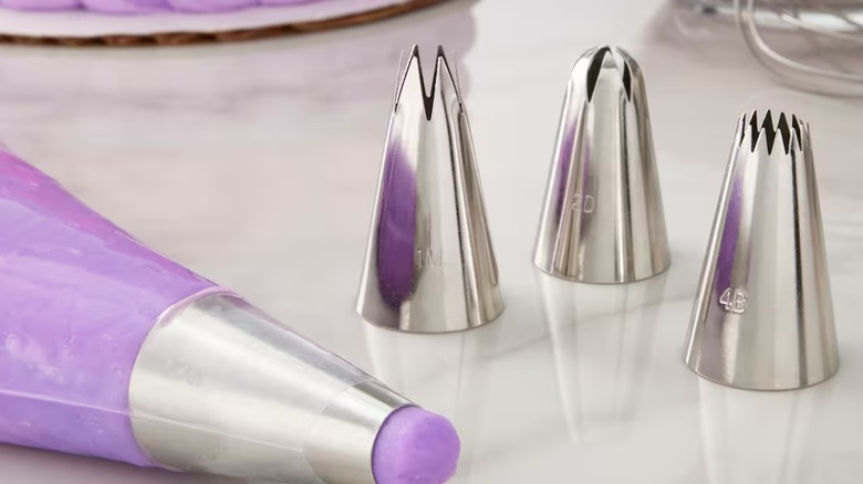 plastic pastry bag with purple icing next to three metal decorating tips