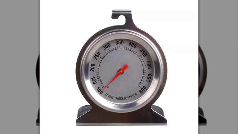 Silver metal oven thermometer with red dial on white background