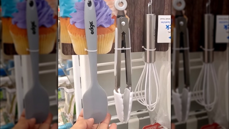 set of spatula, tongs, whisk in packaging  on display in a store being touched by a hand