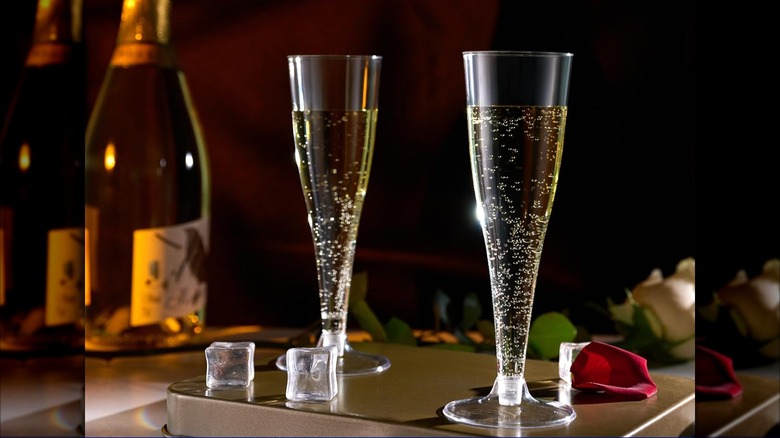 Product image of two filled JOLLY CHEF Plastic Champagne Flutes on a table next to a bottle of Champagne