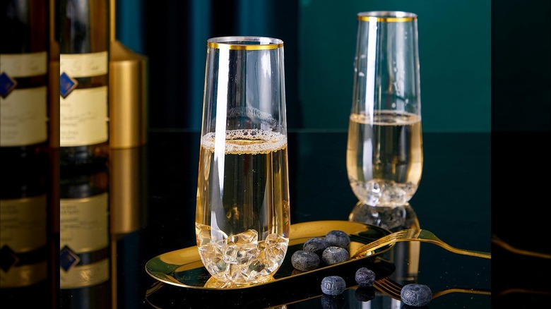 Product image of N9R Plastic Stemless Champagne Flutes filled on a table next to blueberries and a Champagne bottle in the background.