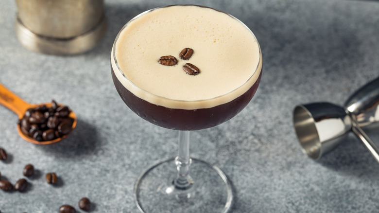 A glass of espresso martini with coffee beans on counter