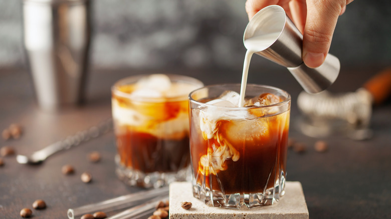 Hand pouring cream into white Russian cocktail