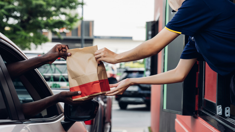A McDonald's worker hands a bag of food to a customer at the drive-thru