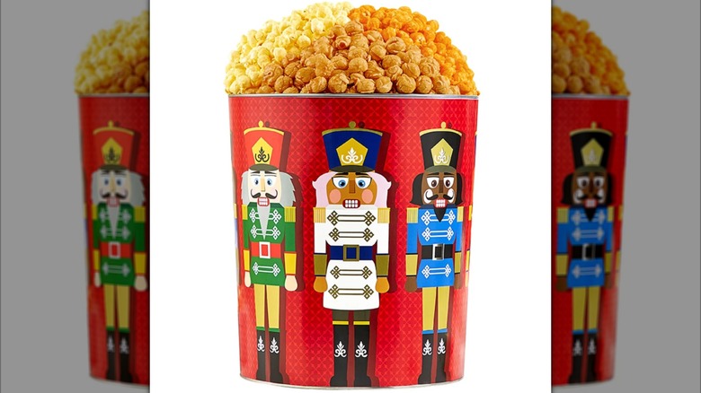 A large red metal tin with nutcracker designs on it, overflowing with popcorn