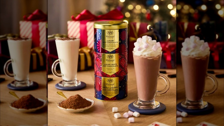 Three tins of hot chocolate mixed stacked up, with two of the hot chocolates in nearby glasses