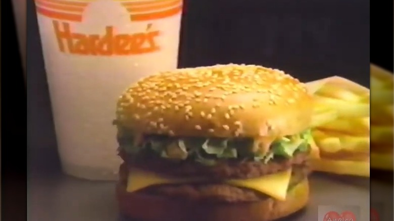 A still from a vintage Hardee's Big Twin Burger commercial, showing the burger with fries and a drink on a black background