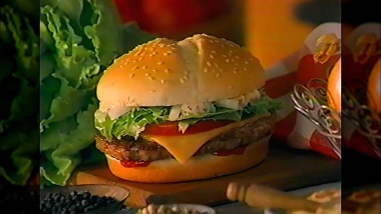 A still from a 1990s ad for the McDonald's Arch Deluxe burger; the burger is on a cutting board next to a head of lettuce and other burger ingredients