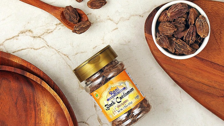 Bottle of Rani black cardamom with black cardamom in a bowl and wooden spoon