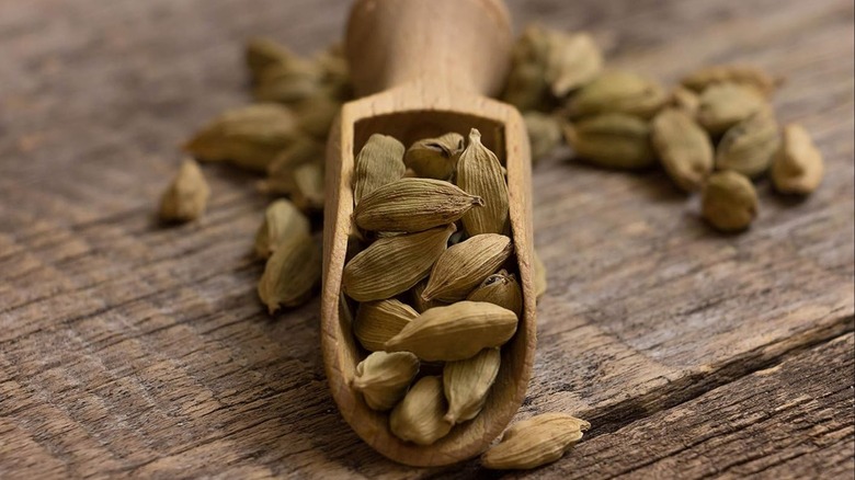 A wooden scoop with cardamom pods on a wood table