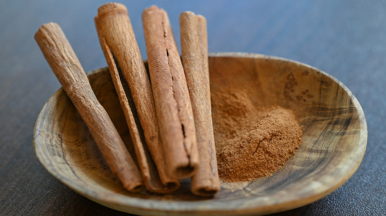 A wooden bowl of ground and whole cinnamon sticks