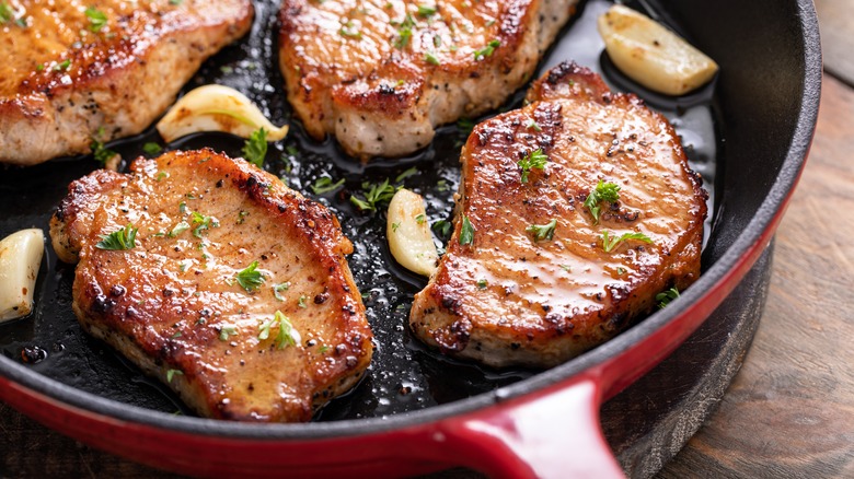 Pork chops frying in pan with garlic and herbs