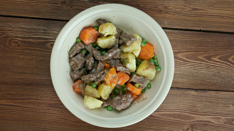 A bowl of scouse stew, with chunks of beef and vegetables, on wooden surface