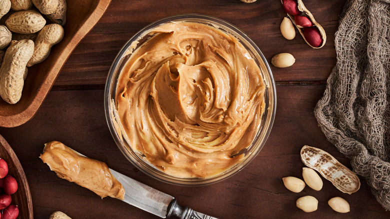 A bowl of peanut butter and whole peanuts on a table