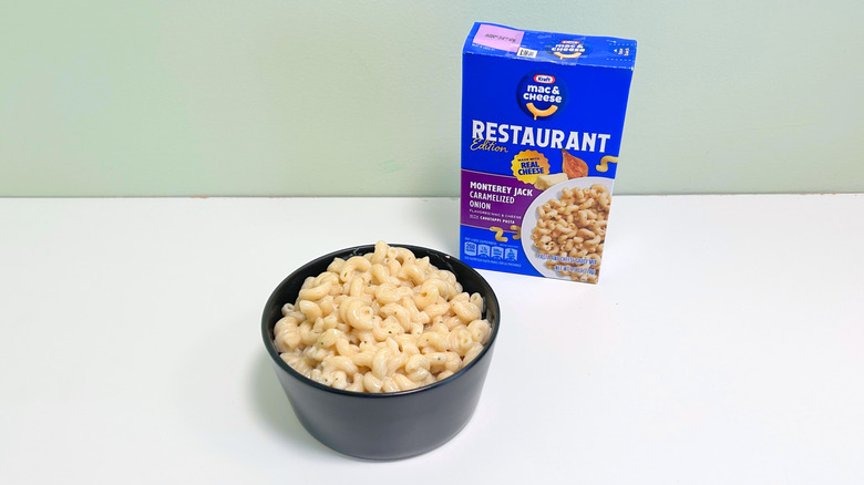 A box of Kraft Restaurant Edition Monterey Jack Caramelized Onion Mac and Cheese next to a bowl of mac and cheese