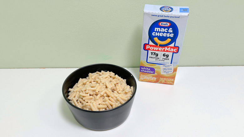 A box of Kraft PowerMac White Cheddar Mac and Cheese next to a  bowl of mac and cheese
