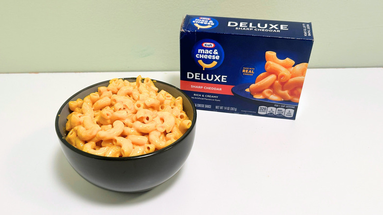 A box of Kraft Deluxe Sharp Cheddar Mac and Cheese next to a bowl of mac and cheese