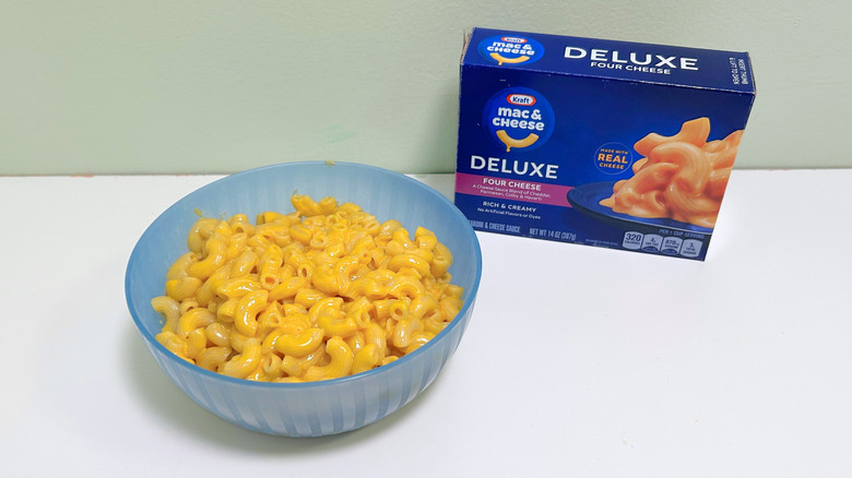A box of Kraft Deluxe Four Cheese Mac and Cheese next to a bowl of mac and cheese