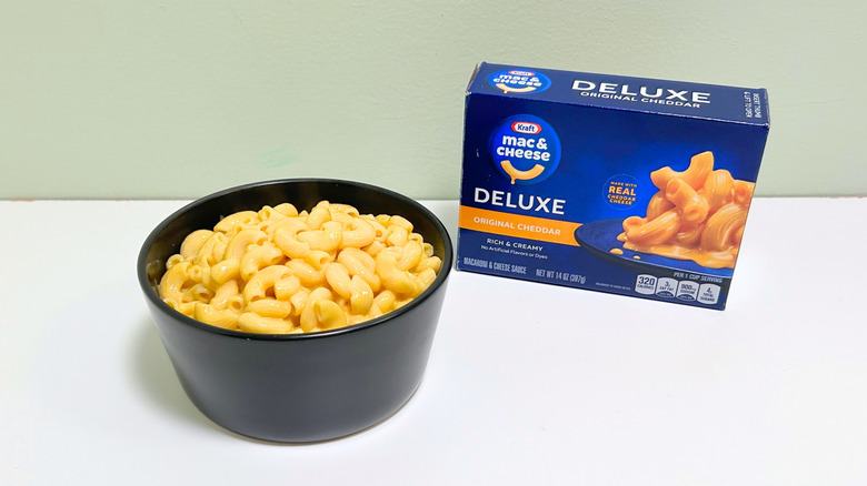 A box of Kraft Deluxe Original Cheddar Mac and Cheese next to a bowl of mac and cheese