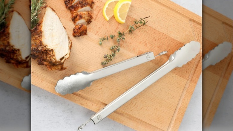 Tongs on cutting board with chicken