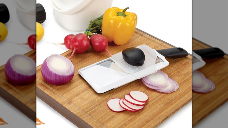 Product image of the OXO Good Grips Handheld Mandoline Slicer with red onions, radishes and yellow bell pepper.