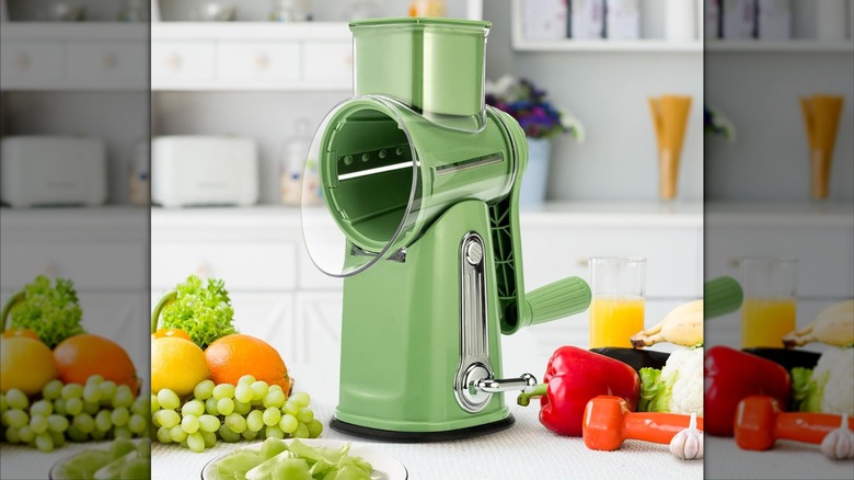 Product image of the SUSTEAS Rotary Cheese Grater in green with assorted produce on the counter around it.