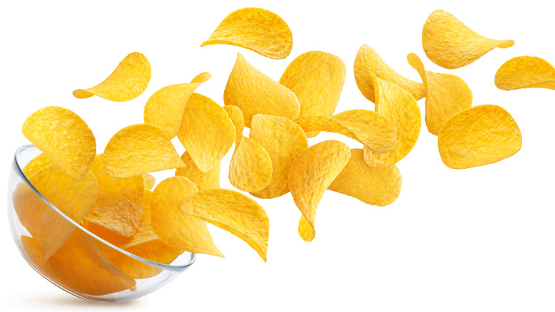 Potato chips falling into glass bowl 