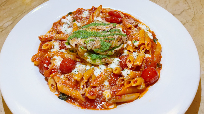 A bowl of tomato basil pasta with grilled chicken and lines of pesto
