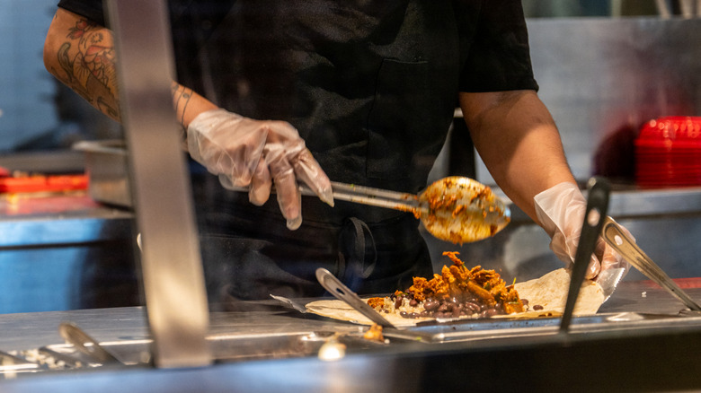 A Chipotle employee adds meat to a burrito