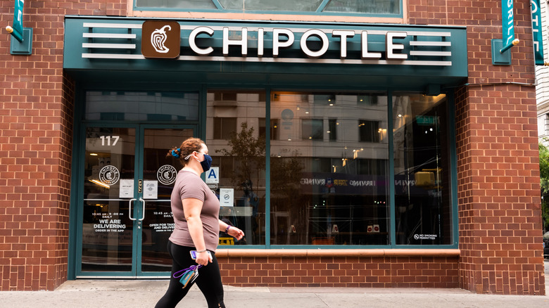 A person wearing a face mask walks past a Chipotle