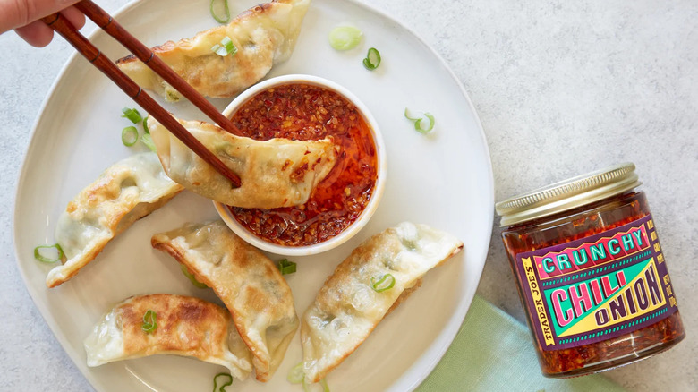 Chopsticks dipping potsticker into crunchy chili onion oil