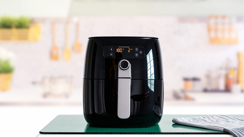 Black air fryer in white kitchen wood utensils
