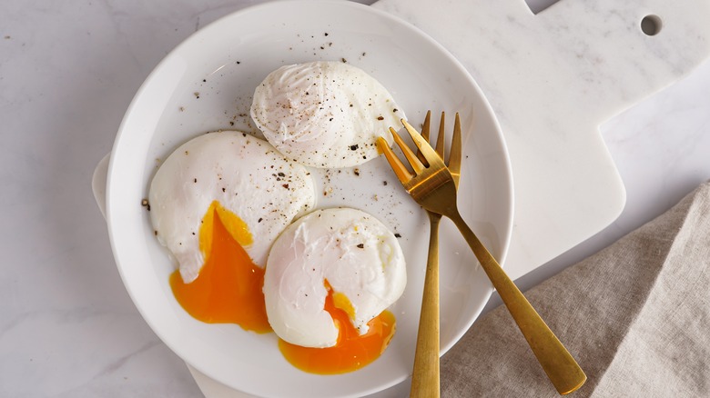 White plate of poached eggs with golden forks