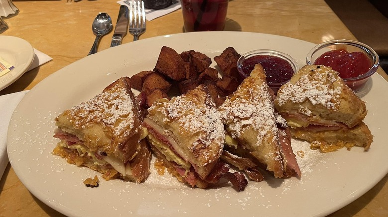 Close-up on a plate of Cheesecake Factory's Monte Cristo sandwich cut into slices and served with potatoes