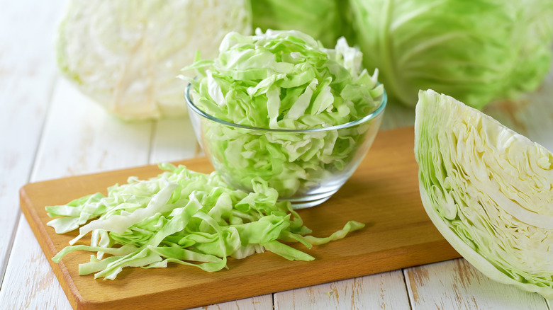 Sliced cabbage next to uncut cabbage on a wooden surface
