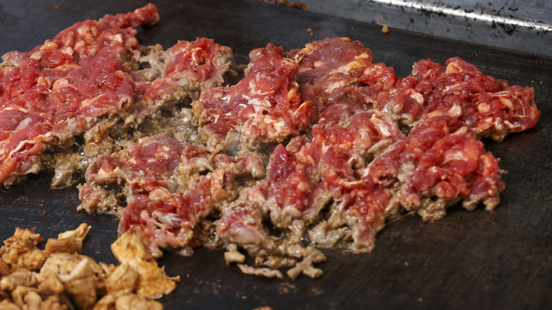 Cheesesteak meat cooks on a flat top grill