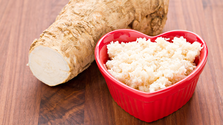 Close up of a heart-shaped bowl of freshly prepared horseradish next to a horseradish root